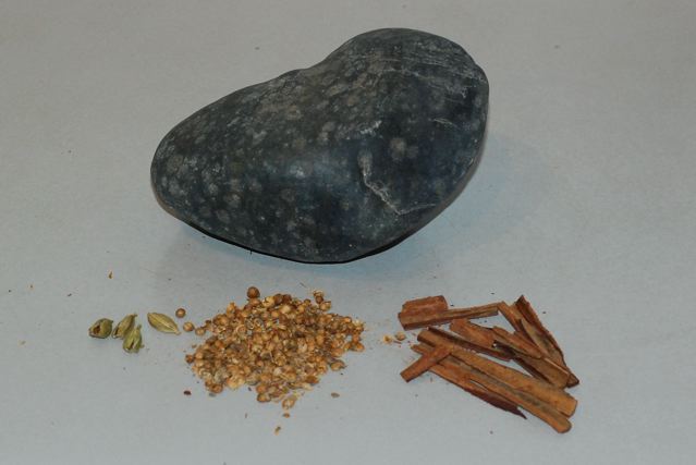 Cardamom pods, coriander seeds, and cinnamon stick after being smashed with a rock