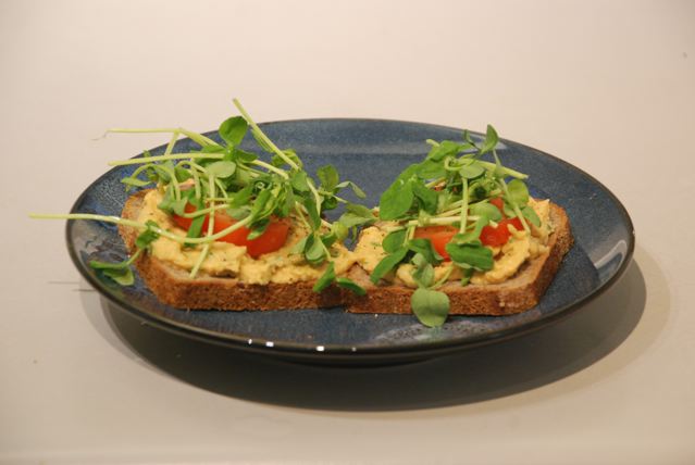 Sandwhich of gluten free bread topped with Roasted Garlic and Eggplant Hummus, tomato, and  peas shoots