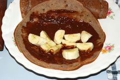 Crepe with sauce spread over and topped with sliced bananas ready to be rolled into cigar shape