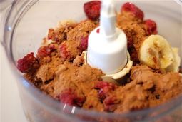 Bananas, raspberries, cocoa powder, vanilla, and maple syrup in a food processor waiting to be blended