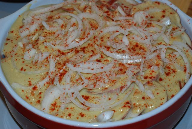 Top layer of potatoes covered in sauce, onions and sprinkled paprika