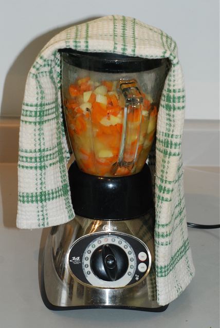 Hot vegetables in a blender with a towel on top