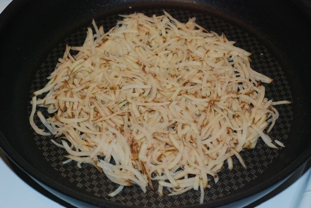 Shredded potato spread out evenly in the non-stick pan